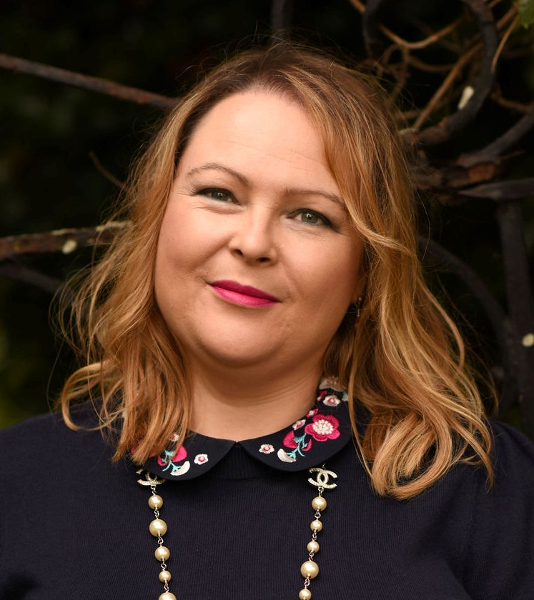 A picture of Claire Bradley - a white woman with blonde hair wearing a navy shirt with a coloured collar and a string of pearls