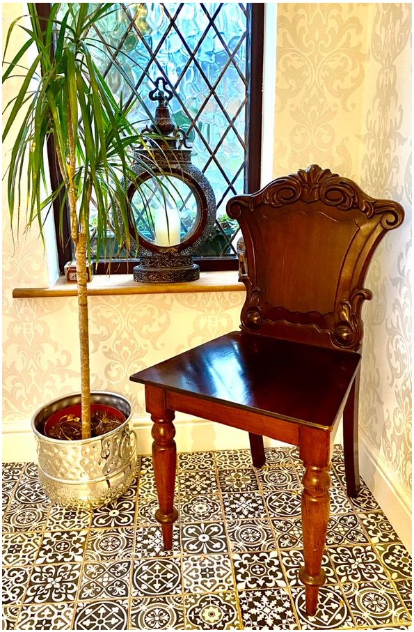 A mahogany chair and plant pot in a hallway with a tiled floor and a window in the background